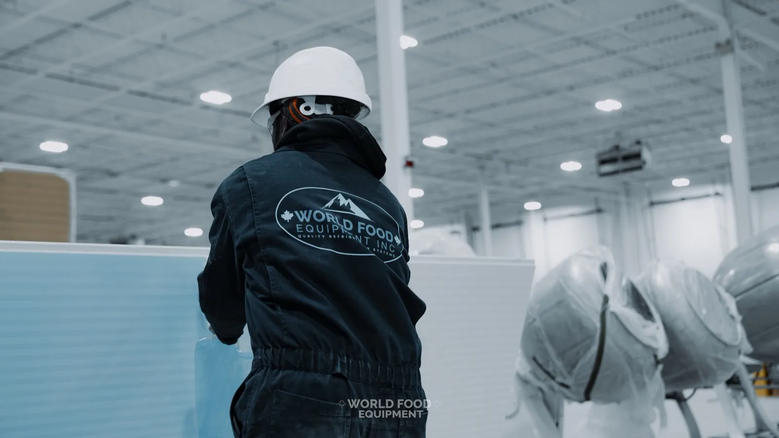 WFE crew member in branded coveralls and hard hat carrying an insulated walk-in panel during an Ontario install